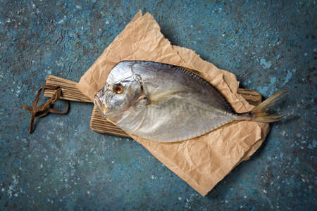 Top view of tasty salty dried sea fish vomer or Selena on wooden cutting board and blue concrete backgroundの写真素材