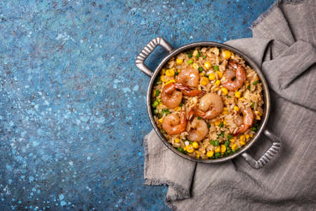 Top view of frying pan with chinese rice, tasty prawns, yellow corn, chicken eggs and green onion on grey linen cloth and blue concrete background with copy spaceの写真素材