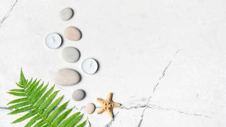 Spa concept. Top view of grey sea stones and aroma candles on white marble background with copy...