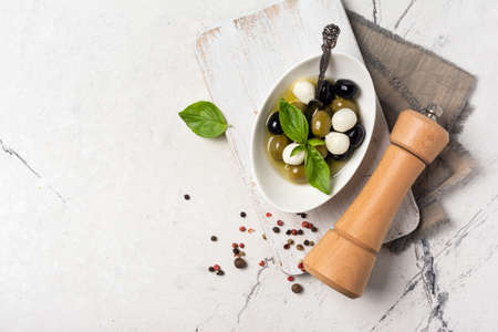 Top view of tasty mix green and black olives with with mozzarella, basil leaves, wooden pepper mill on white marble background with copy spaceの写真素材