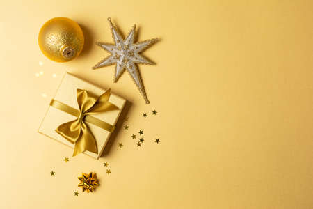 Decorations for the New Year's party. Beautiful golden gift box with shiny satin bow for present and toys for christmas tree on gold background with copy spaceの写真素材
