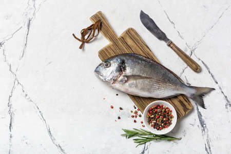 Top view of fresh fish dorado or gilt-head bream with spices as pepper, rosemary on wooden cutting...