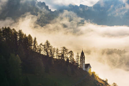 Picturesque landscape of foggy morning in La Valle Wengen mountain village with church in Dolomites Alpsの写真素材