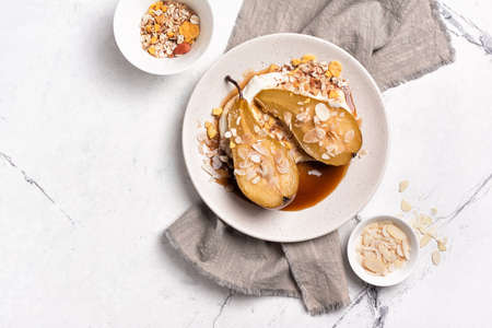 Top view of fruit dessert with baked pears, caramel sauce, cheese cream and almond flakes on white marble background with copy spaceの写真素材