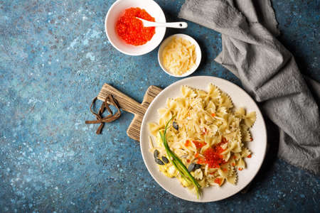 Top view of tasty farfalle pasta with red caviar, cheese, green onion, pumpkin seeds, pine nuts and sauce on blue concrete backgroundの写真素材