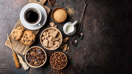 Top view of bowls with brown lump and granulated cane sugar, crystal sugar sticks, coffee beans,...