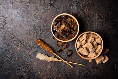 Top view of bowls with brown cane lump sugar and cristal sugar stick on dark concrete backgroundの写真素材