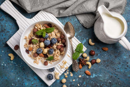 Top view of oatmeal with milk, fresh blueberry, almonds, hazelnuts and cashews nuts, green mint leaves for healthy breakfast on blue concrete backgroundの写真素材