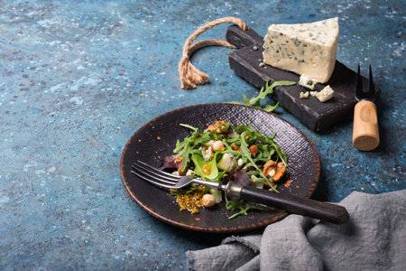 Healthy and tasty vegetarian food. Salad with mix of fresh green leaves, blue cheese, nuts and mustard sauce on blue concrete backgroundの写真素材