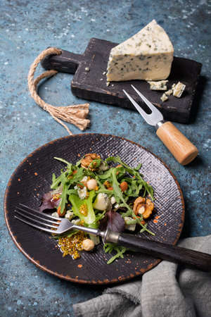 Healthy and tasty vegetarian food. Salad with mix of fresh green leaves, blue cheese, nuts and mustard sauce on blue concrete backgroundの写真素材