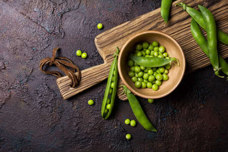 Top view of fresh green peas in bowl for healthy nutrition on wooden cutting board and brown conctrete backgroundの写真素材