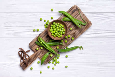 Top view of fresh green peas in bowl for healthy nutrition on wooden cutting board and white backgroundの写真素材