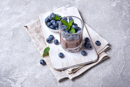 Tasty chocolate pudding or sweet mousse with blueberry and mint in portion glass on white wooden board and grey concrete backgroundの写真素材