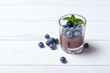 Tasty chocolate pudding or sweet mousse with blueberry and mint in portion glass on white wooden background. Space for textの写真素材