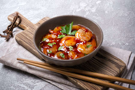Bowl with spicy shrimps in sweet chili asian red sauce with chopsticks on grey concrete backgroundの写真素材