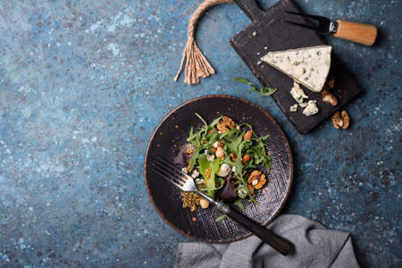 Top view of healthy and tasty vegetarian food. Salad with mix of fresh green leaves, blue cheese, nuts and mustard sauce on blue concrete backgroundの写真素材