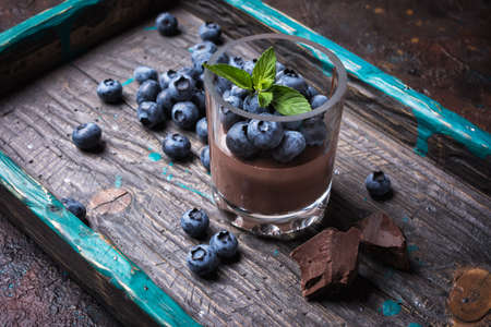 Tasty chocolate pudding or sweet mousse with blueberry and mint in portion glass on wooden tray and dark concrete backgroundの写真素材
