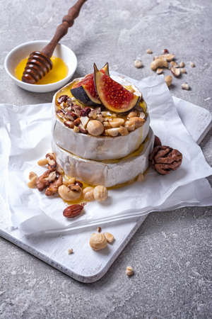 Gourmet appetizer of white brie cheese or camembert with fresh figs, nuts and honey on grey concrete...