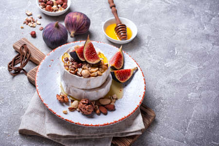 Gourmet appetizer of white brie cheese or camembert with fresh figs, nuts and honey on gray concrete backgroundの写真素材