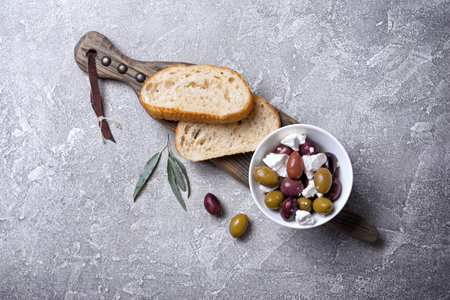 Top view of tasty olives mix with Feta cheese and slices of bread on grey concrete backgroundの写真素材