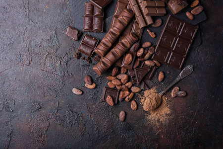 Pieces of broken tasty milk and dark chocolate bars with cocoa beans on brown concrete backgroundの写真素材