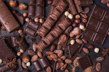 Pieces of broken tasty milk and dark chocolate bars with cocoa beans and hazelnut on brown concrete backgroundの写真素材