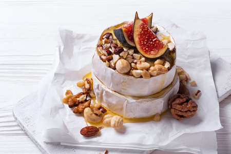Gourmet appetizer of brie cheese or camembert with fresh figs, nuts and honey on white wooden backgroundの写真素材