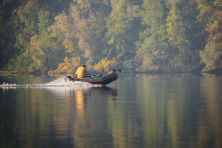 Green inflatable rubber motor boat floating on the river for fishing on autumn trees background