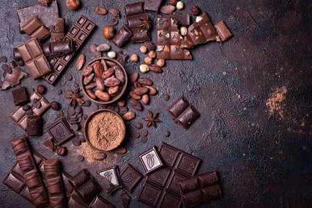 Pieces of broken tasty milk and dark chocolate bars with cocoa beans, hazelnut and powder on black...