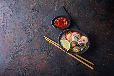 Top view of bowl with japanese bean or glass noodles, tasty shrimps, shiitake mushrooms, green onion and red pepper on dark concrete backgroundの写真素材