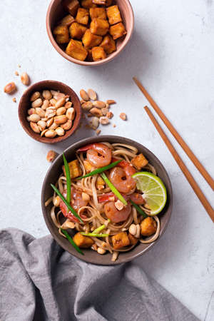 Top view of plate with asian udon noodles, spicy shrimps, fried tofu cheese, peanuts, lime and green onion on white marble backgroundの写真素材
