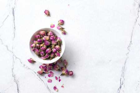 Top view of bowl with dried rose buds for fragrant tea on white marble background with copy spaceの写真素材