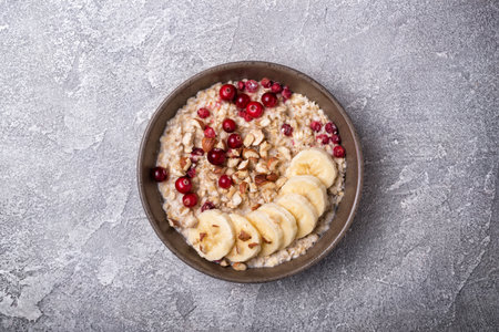 Top view of oatmeal with fresh cranberry, hazelnuts and banana slices for healthy breakfast on grey concrete backgroundの写真素材