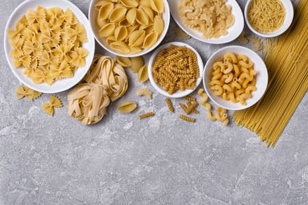 Top view on variety of italian raw pasta in white bowl on grey concrete backgroundの写真素材