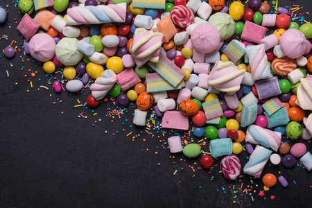 Multicolored sweet and bright dragee, candies, lollipops, marshmallows for fun party on black marble...