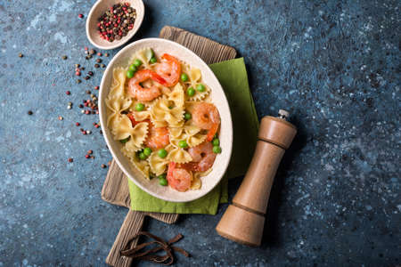 Top view of tasty italian farfalle pasta with shrimps or prawn and green peas on blue concrete backgroundの写真素材