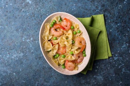 Top view of tasty italian farfalle pasta with shrimps or prawn and green peas on blue concrete backgroundの写真素材