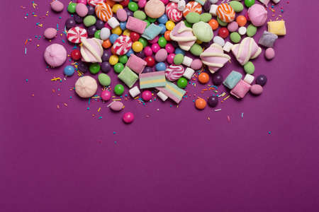 Multicolored sweet and bright dragee, candies, lollipops, marshmallows for fun party on purple backgroundの写真素材