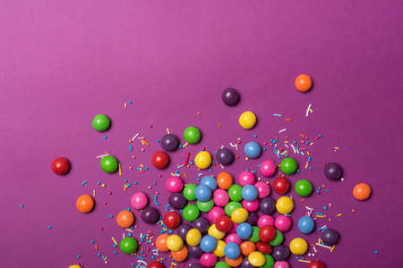 Multicolored glaze dragee or candies for fun party on purple background