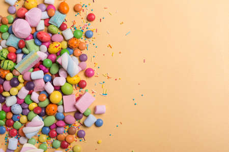 Multicolored sweet and bright dragee, candies, lollipops, marshmallows for fun party on golden backgroundの写真素材