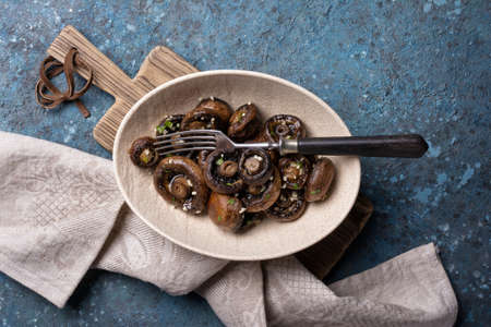 Top view of grilled champignon mushrooms in bowl with spice on blue concrete backgroundの写真素材