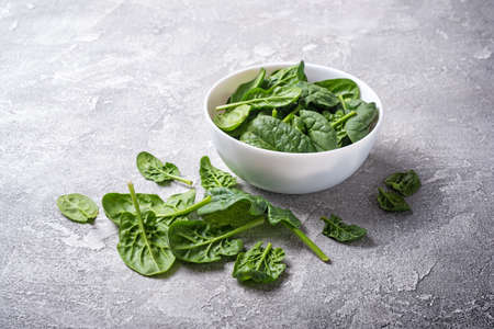 Bowl with green fresh baby spinach on grey concrete background