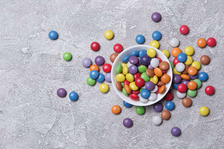 Chocolate multicolored glaze dragee or candies in white bowl on grey concrete backgroundの写真素材