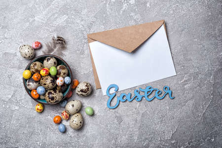 Top view of small quail eggs, colored candies and mock-up of blank white card for Easter on grey concrete backgroundの写真素材