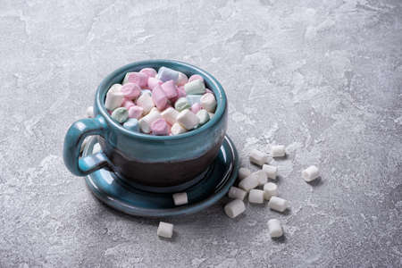 Big blue cup with mini colored marshmallows for hot chocolate, cocoa, fun party on grey concrete...