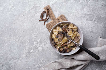 Top view of tasty italian farfalle pasta and champignon mushrooms with cream sauce in bowl on grey concrete backgroundの写真素材