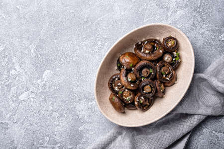 Top view of grilled champignon mushrooms in bowl with spice on grey concrete background with copy spaceの写真素材