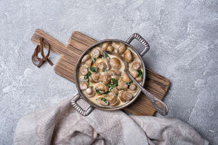 Top view of champignon mushrooms in frying pan with spinach leaves and cream sauce on grey concrete backgroundの写真素材