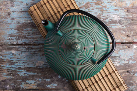 Traditional green asian cast iron kettle on bamboo mat and old blue wooden backgroundの写真素材