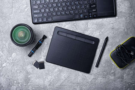 Top view of photographer work place with graphics tablet, keyboard, lens and portable hard drive on...
